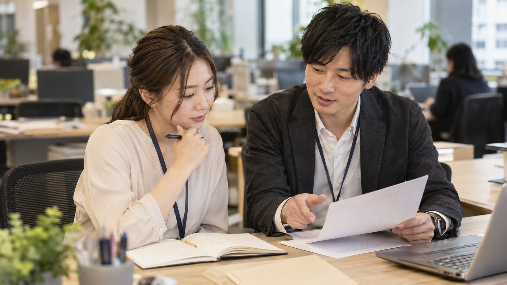 机上の資料を見ながら業務の進め方を相談する二人